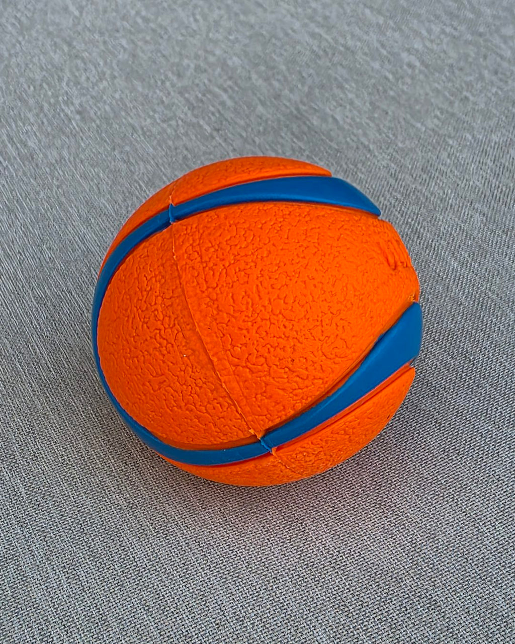 Orange and blue striped rubber ball on gray fabric