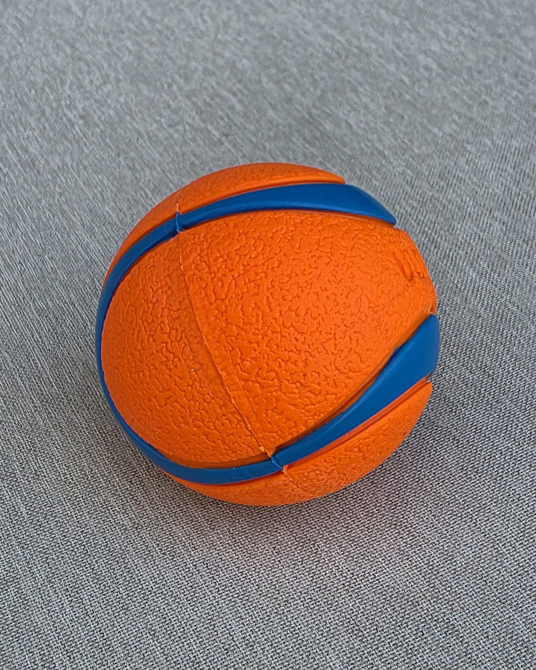 Orange and blue striped rubber ball on gray fabric