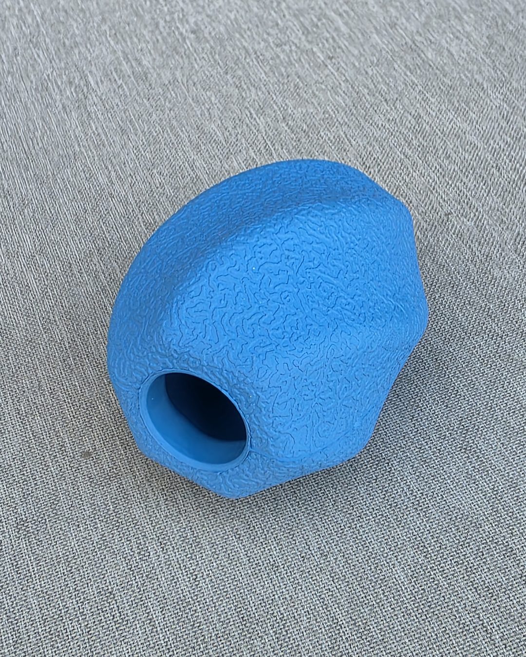 Blue textured rubber treat toy with a hole for treats, on gray fabric