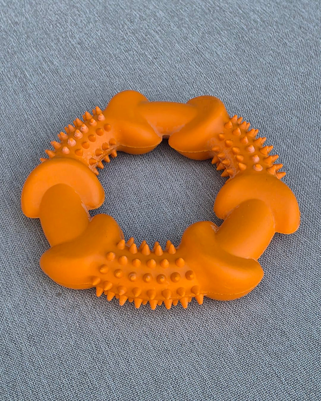 Orange spiky rubber chew ring on gray fabric