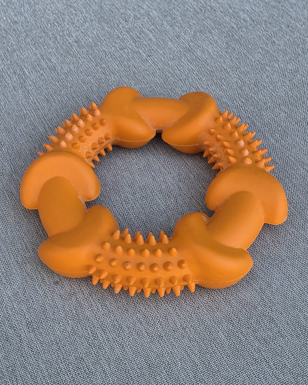 Orange spiky rubber chew ring on gray fabric